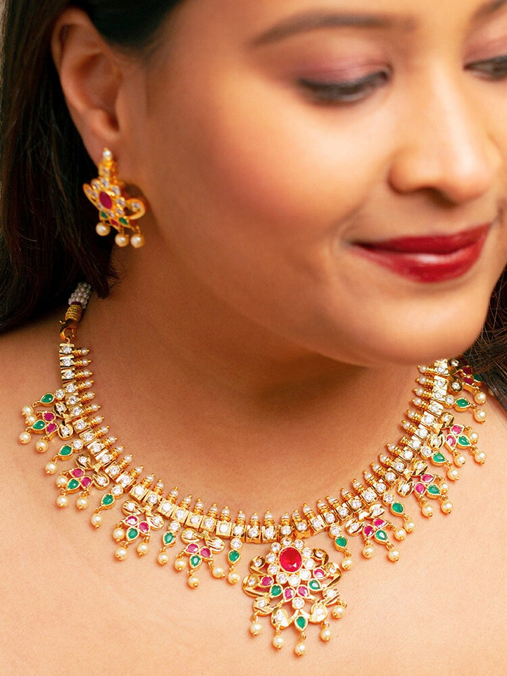 Close-up of a woman wearing an ornate traditional (Gold Polish) Collar jewellery set and earrings with pearls, ruby &amp; Emerald Colored Stone and American Diamond. Festive Diwali outfit styled with an American diamond artificial necklace. Close-up shot of a high-quality American diamond artificial necklace worn for festive celebrations.