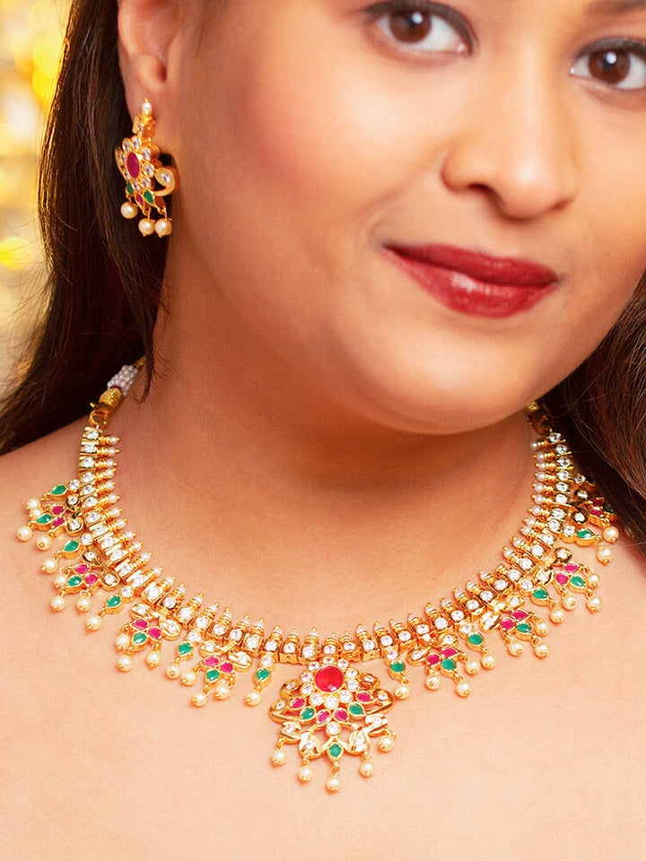 Close-up of a woman wearing an ornate traditional (Gold Polish) Collar jewellery set and earrings with pearls, ruby &amp; Emerald Colored Stone and American Diamond. Festive Diwali outfit styled with an American diamond artificial necklace. Close-up shot of a high-quality American diamond artificial necklace worn for festive celebrations.