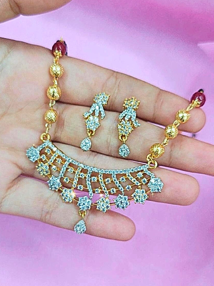 A hand holds the Priyanshi Mangalsutra—a gold necklace with black mangalsutra beads and matching earrings, pendant featuring sparkling American Diamonds—set against a soft pink background, perfect for your wedding ceremony dress. Diamond mangalsutra. Modern mangalsutra. 