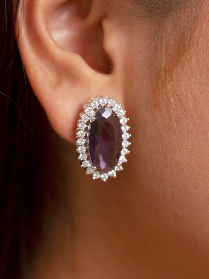 Close-up of a woman wearing an ornate Western (Silver Polish) Purple Pendant set and Earrings with American Diamond and Purple Colored Stone. Close-up of a cocktail party look featuring a premium Colored Stone Pendant Set. Party wear outfit completed with a lightweight Colored Stone Pendant set.