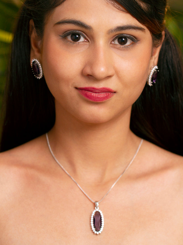 Close-up of a woman wearing an ornate Western (Silver Polish) Purple Pendant set and Earrings with American Diamond and Purple Colored Stone. Close-up of a cocktail party look featuring a premium Colored Stone Pendant Set. Party wear outfit completed with a lightweight Colored Stone Pendant set.