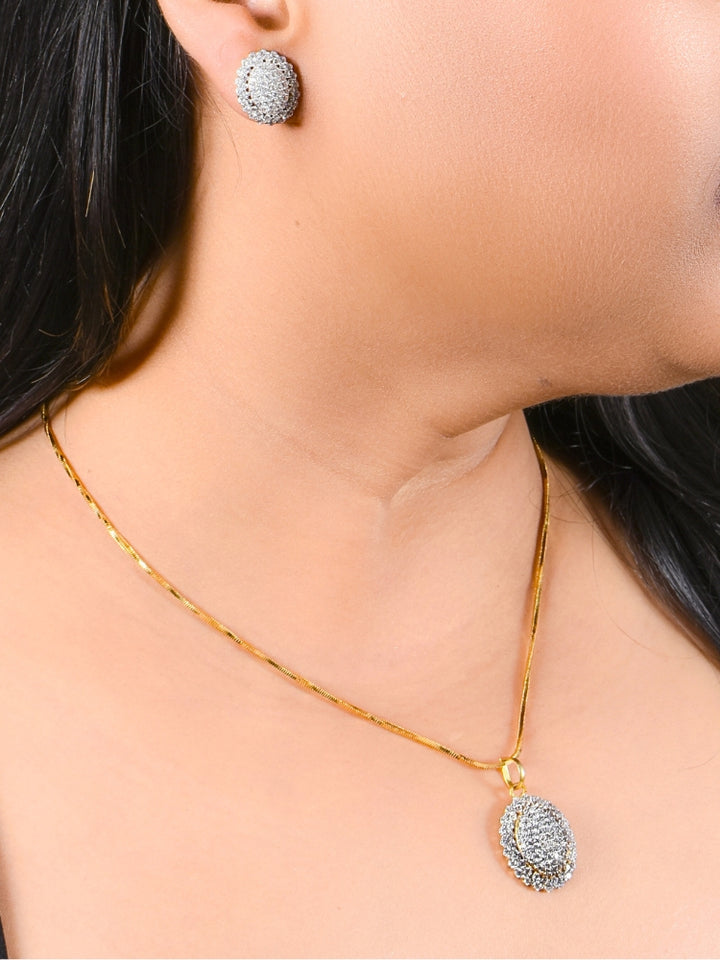 A woman wears the Rachel Pendant Set—a  pendant set with gold chain and an oval pendant with american diamonds and matching round stud earrings. The jewelry stands out beautifully against her skin and dark hair.