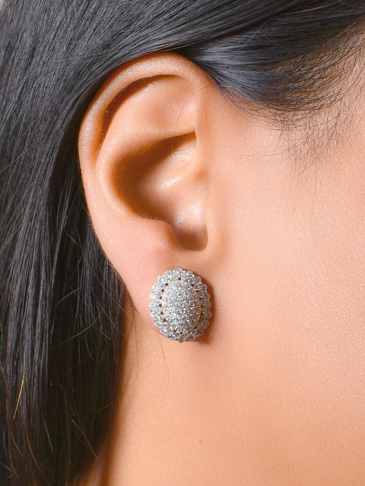 A woman wears the Rachel Pendant Set—a  pendant set with gold chain and an oval pendant with american diamonds and matching round stud earrings. The jewelry stands out beautifully against her skin and dark hair.