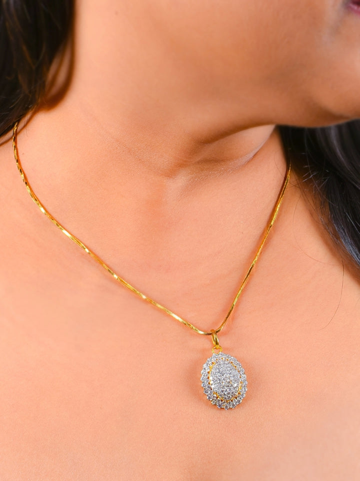 A woman wears the Rachel Pendant Set—a  pendant set with gold chain and an oval pendant with american diamonds and matching round stud earrings. The jewelry stands out beautifully against her skin and dark hair.