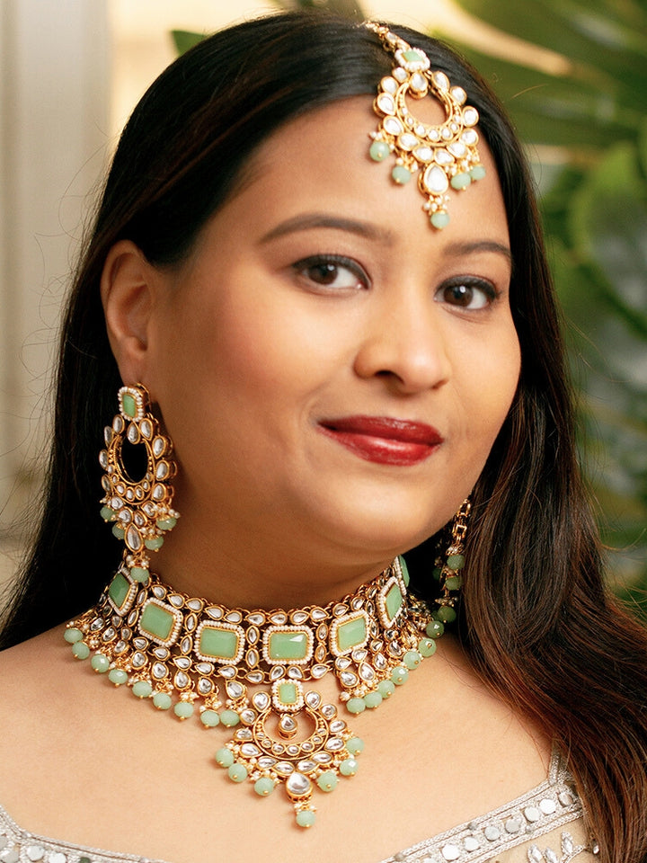 Close-up of a woman wearing an ornate traditional Green Kundan Choker jewellery set and earrings and maangtikka with Kundan, Mint green Stone, Pearls and Mint Green Crystal Beads. Bride wearing a royal Kundan artificial necklace for wedding rituals. Wedding celebration look enhanced with a statement Kundan necklace. 