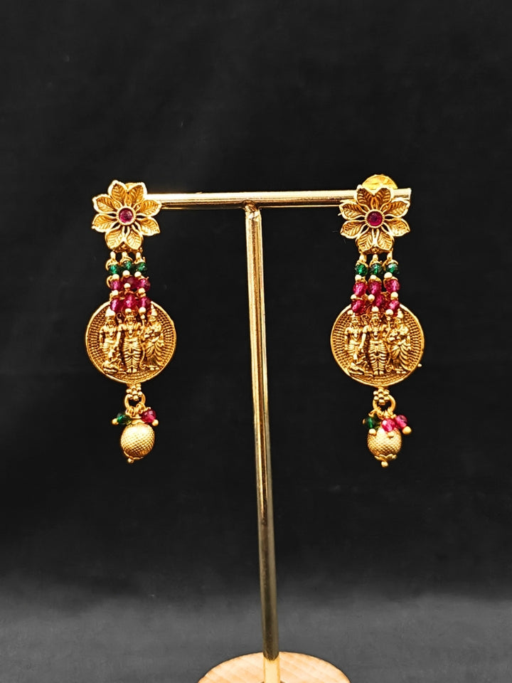 The Raghav Necklace Set featuring a traditional gold Collar Red & Green necklace and matching earrings with Goddess Ram in the middle, along with Red and green Colored Stone and Cyrstal Beads. Close-up of a temple imitation necklace styled with a silk saree. Festive Diwali look completed with a traditional temple necklace set.