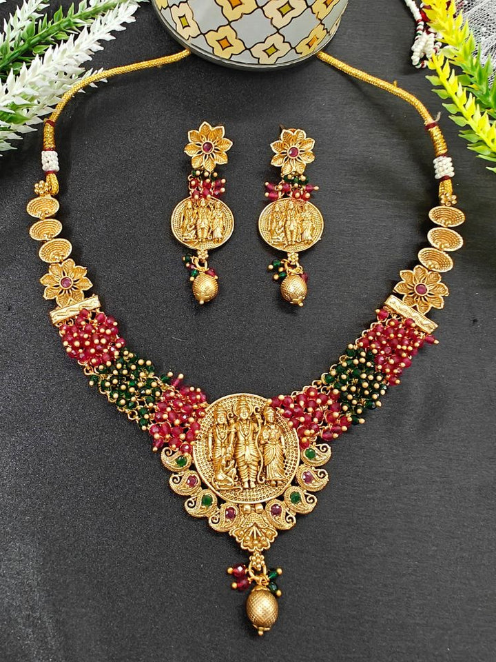 The Raghav Necklace Set featuring a traditional gold Collar Red & Green necklace and matching earrings with Goddess Ram in the middle, along with Red and green Colored Stone and Cyrstal Beads. Close-up of a temple imitation necklace styled with a silk saree. Festive Diwali look completed with a traditional temple necklace set.