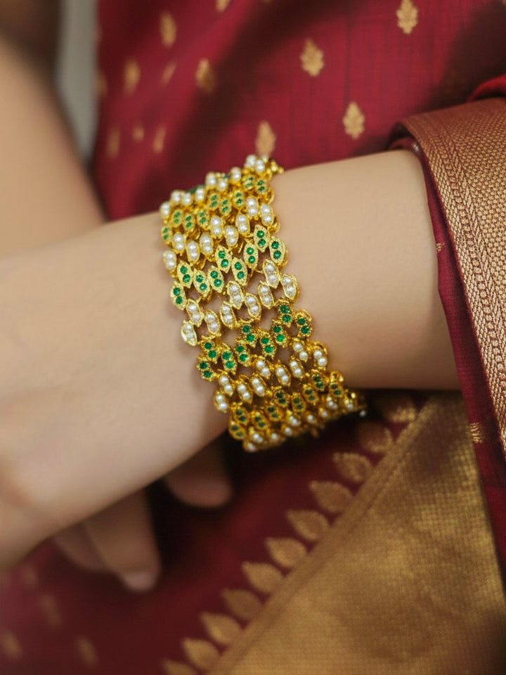 Close-up of a woman wearing an ornate traditional Emerald Green jadau gold Bracelet with pearls and Color Stone. Bride wearing a luxury artificial bracelet for reception night. Close-up of handcrafted artificial bracelet detailing.