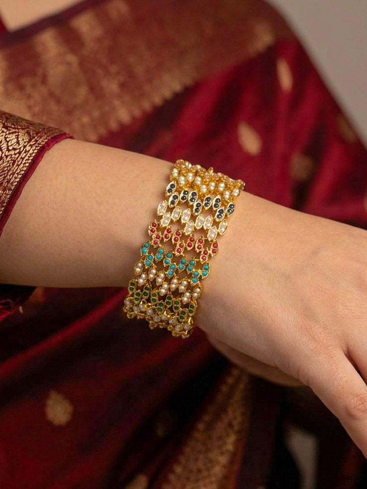 Close-up of a woman wearing an ornate traditional Navratan jadau gold Bracelet with pearls and Color Stone. Festive outfit paired with a premium imitation Jadau bracelet in India. Close-up of a high-quality imitation Jadau bracelet for festive wear.