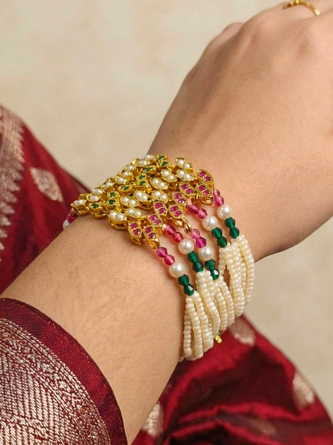 Close-up of a woman wearing an ornate traditional Navratan jadau gold Bracelet with pearls and Color Stone. Festive outfit paired with a premium imitation Jadau bracelet in India. Close-up of a high-quality imitation Jadau bracelet for festive wear.