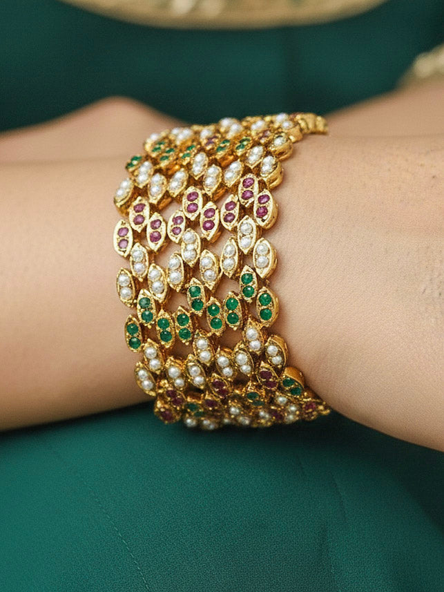 Close-up of a woman wearing an ornate traditional White, Ruby Pink and Green jadau gold Bracelet with pearls and Color Stone. Woman showcasing a premium artificial Jadau bracelet for wedding celebrations. Woman wearing a lightweight Jadau bracelet for long wedding celebrations.