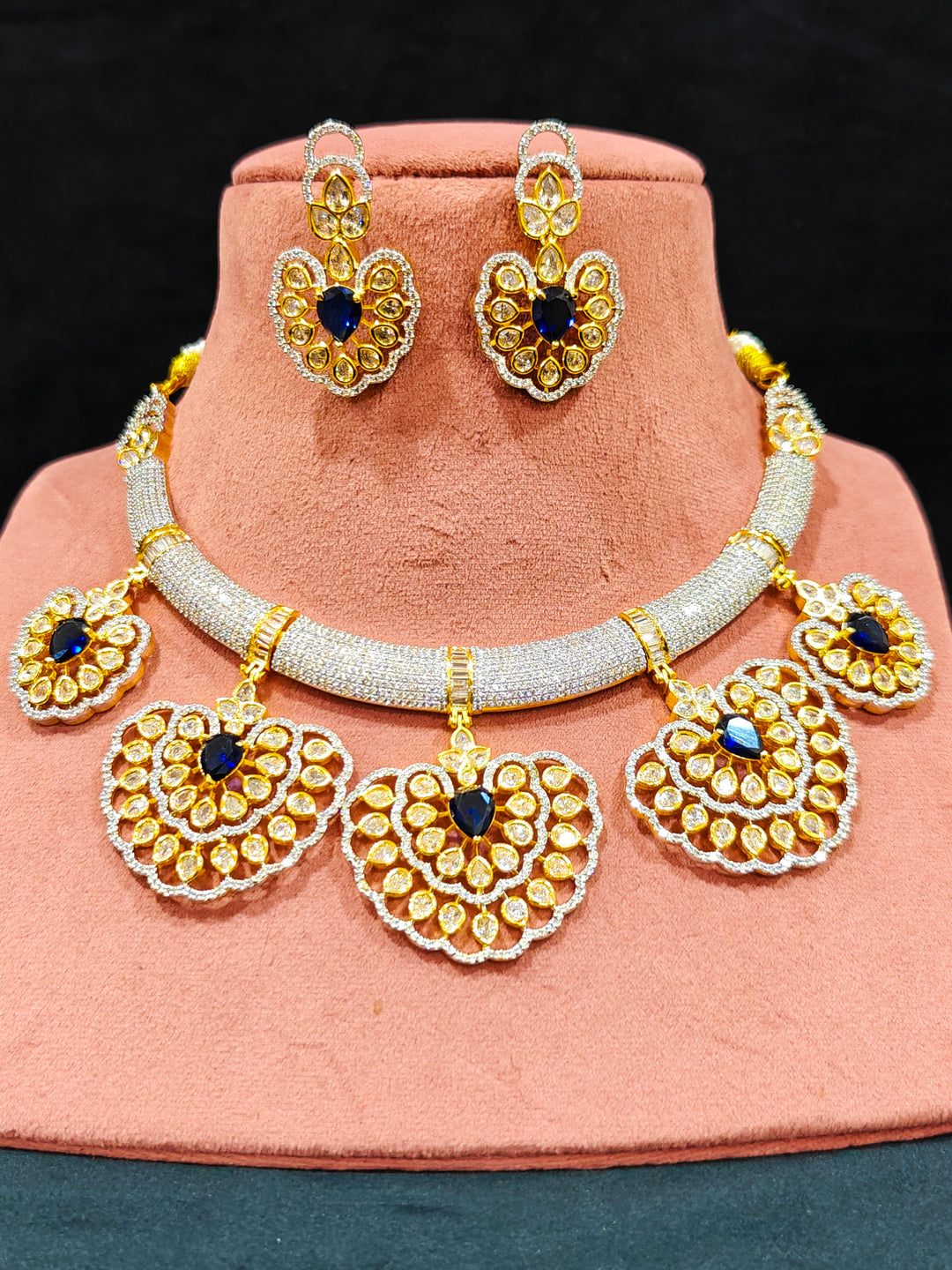 Close-up of an ornate Western American diamond Raizel Blue Necklace Set (Dual Tone) Collar jewellery set and earrings with Colored Stone and American Diamond. Close-up of a cocktail party look featuring a premium American diamond necklace.