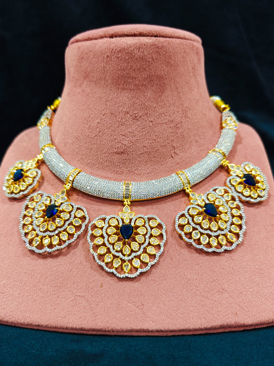 Close-up of an ornate Western American diamond Raizel Blue Necklace Set (Dual Tone) Collar jewellery set and earrings with Colored Stone and American Diamond. Close-up of a cocktail party look featuring a premium American diamond necklace.
