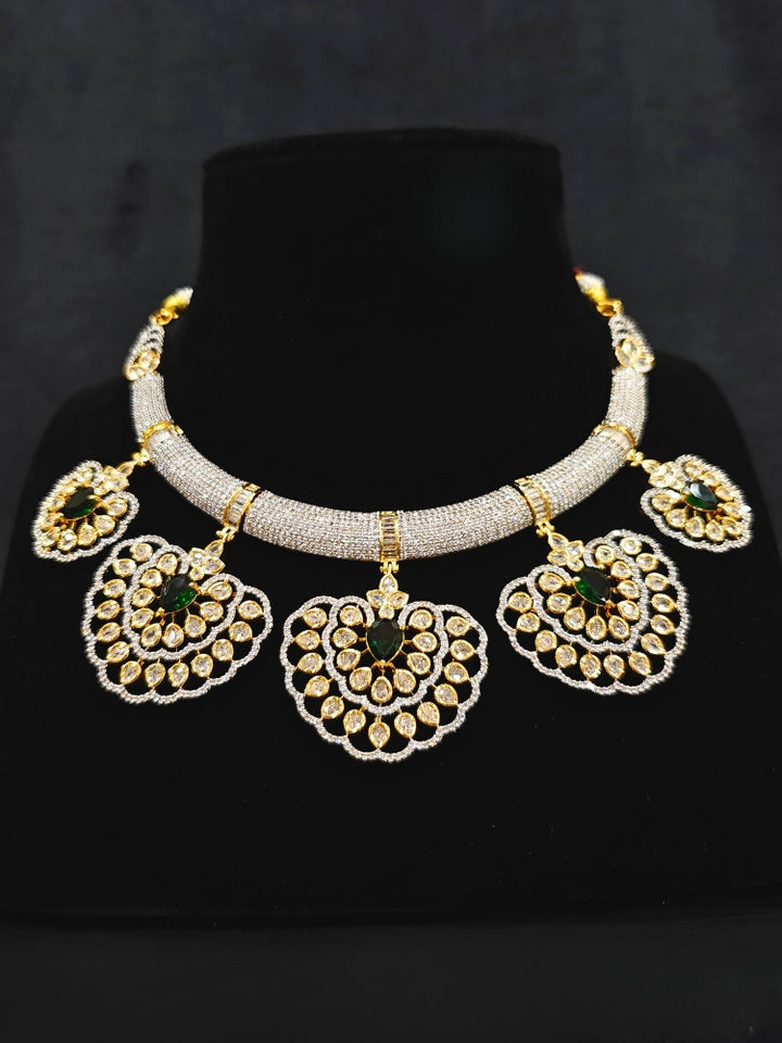 Close-up of an ornate Western American diamond Raizel Emerald Green Necklace Set (Dual Tone) Collar jewellery set and earrings with  Colored Stone and American Diamond. Bride-to-be styled in a premium American diamond artificial necklace for her reception party.