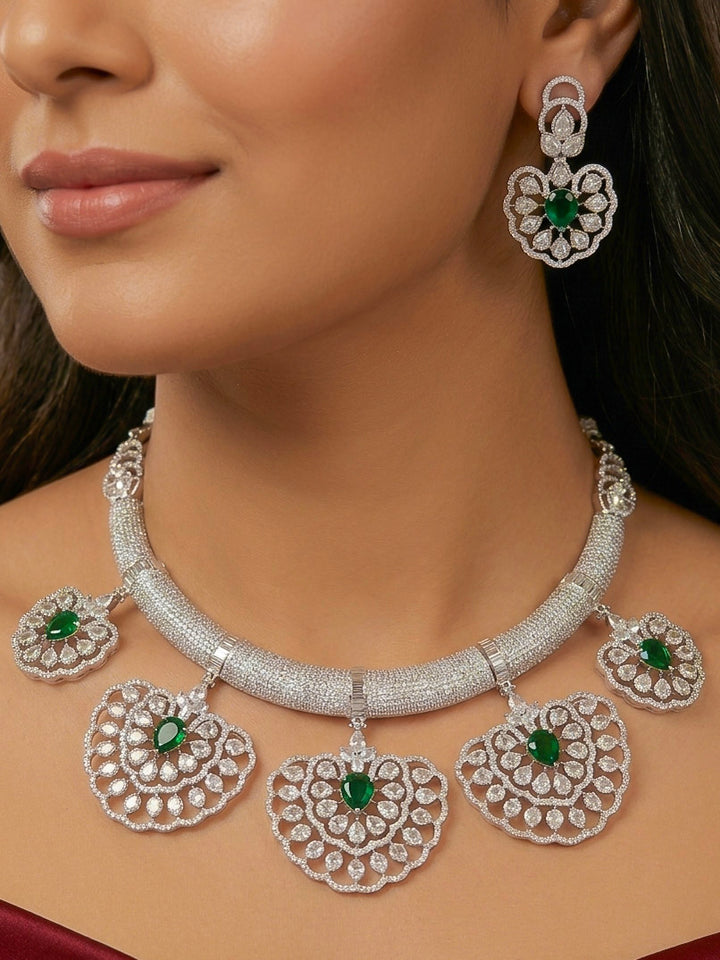 Close-up of a woman wearing an ornate Western American diamond Raizel Emerald Green Necklace Set(Silver Polish) Collar jewellery set and earrings with  Colored Stone and American Diamond. Bride-to-be styled in a premium American diamond artificial necklace for her reception party.