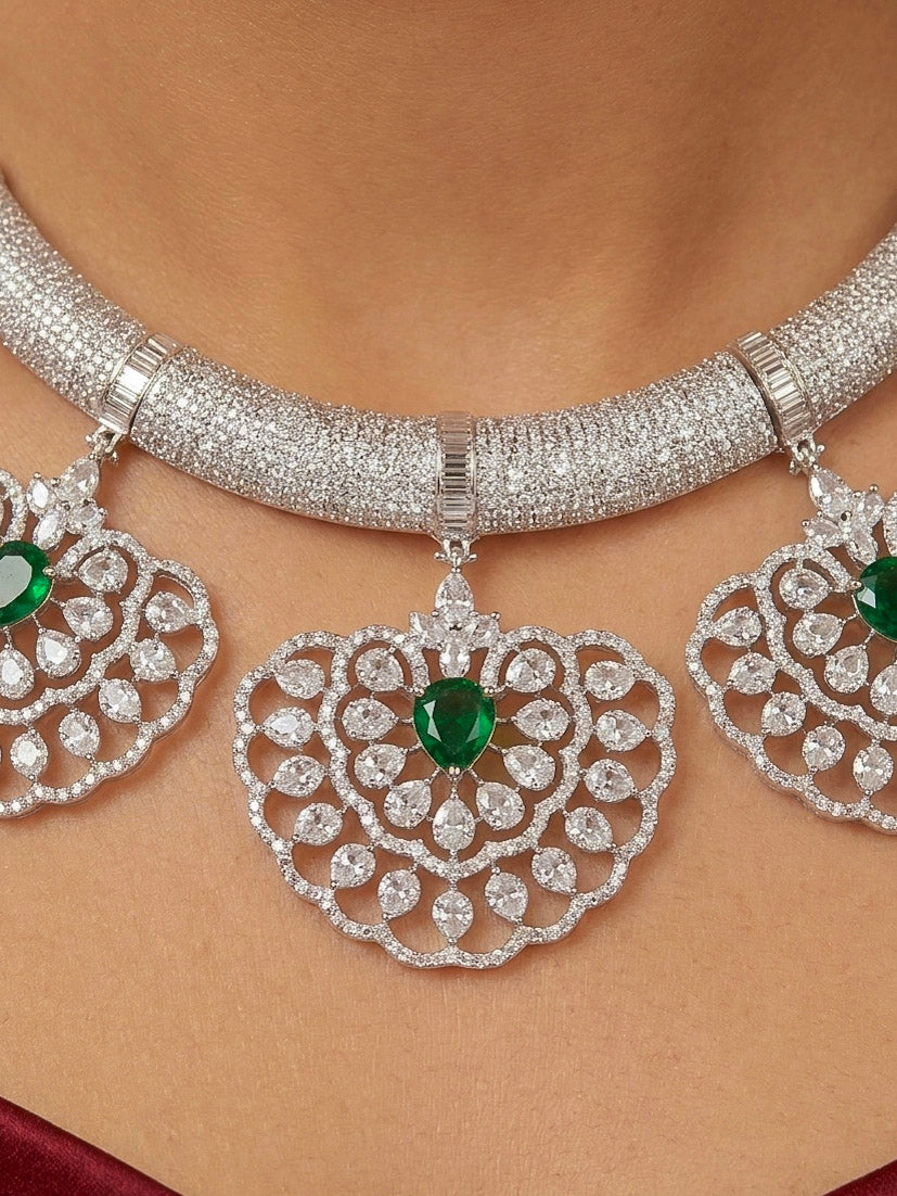 Close-up of a woman wearing an ornate Western American diamond Raizel Emerald Green Necklace Set(Silver Polish) Collar jewellery set and earrings with  Colored Stone and American Diamond. Bride-to-be styled in a premium American diamond artificial necklace for her reception party.