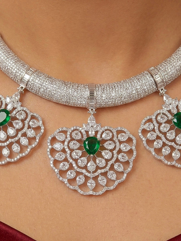 Close-up of a woman wearing an ornate Western American diamond Raizel Emerald Green Necklace Set(Silver Polish) Collar jewellery set and earrings with  Colored Stone and American Diamond. Bride-to-be styled in a premium American diamond artificial necklace for her reception party.