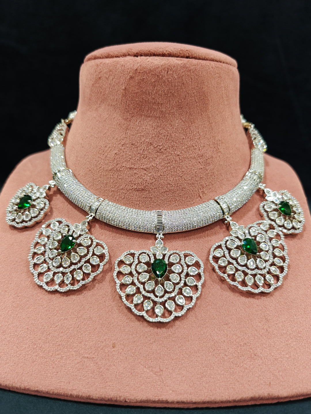 Close-up of a woman wearing an ornate Western American diamond Raizel Emerald Green Necklace Set(Silver Polish) Collar jewellery set and earrings with  Colored Stone and American Diamond. Bride-to-be styled in a premium American diamond artificial necklace for her reception party.