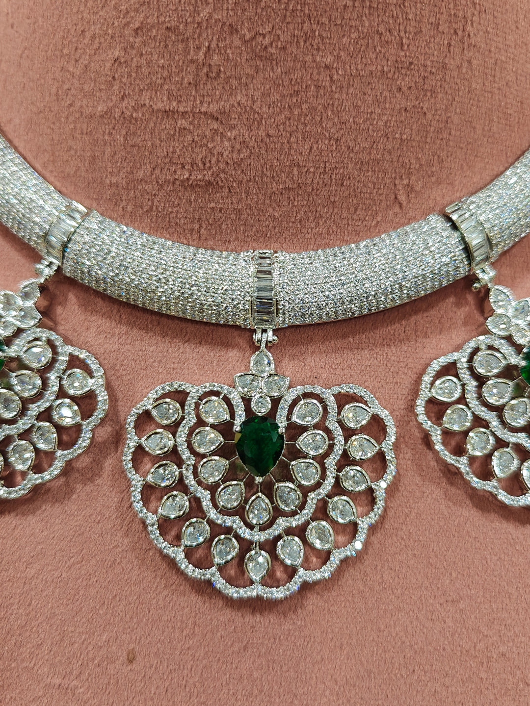 Close-up of a woman wearing an ornate Western American diamond Raizel Emerald Green Necklace Set(Silver Polish) Collar jewellery set and earrings with  Colored Stone and American Diamond. Bride-to-be styled in a premium American diamond artificial necklace for her reception party.
