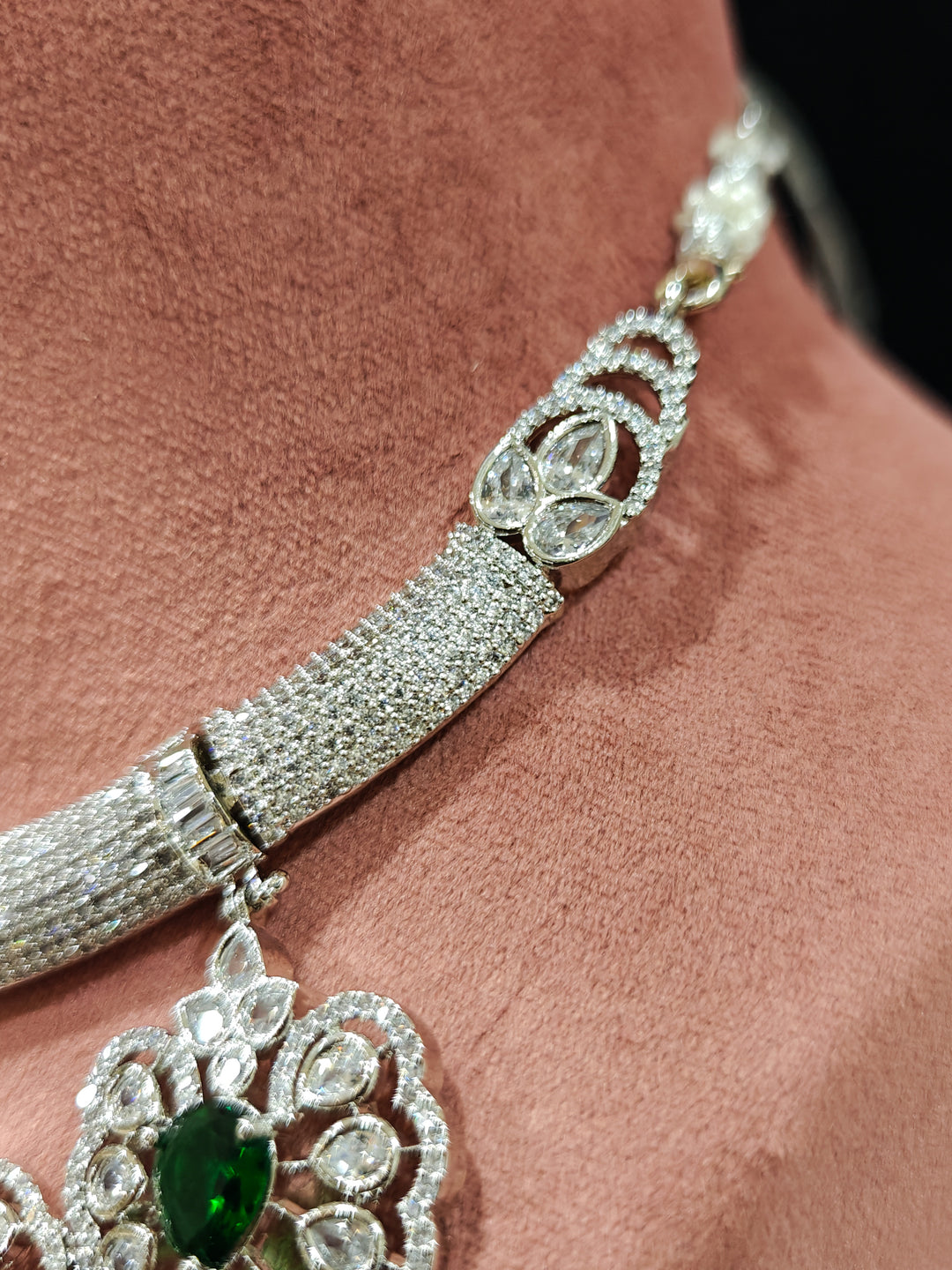 Close-up of a woman wearing an ornate Western American diamond Raizel Emerald Green Necklace Set(Silver Polish) Collar jewellery set and earrings with  Colored Stone and American Diamond. Bride-to-be styled in a premium American diamond artificial necklace for her reception party.