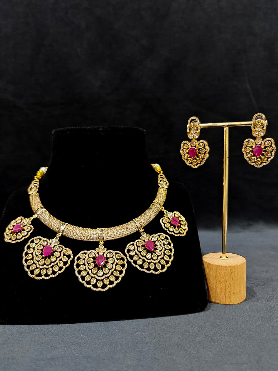 Close-up of an ornate Western American diamond Raizel Ruby Pink Necklace Set (Mehendi Polish) Collar jewellery set and earrings with Colored Stone and American Diamond. Woman styling a statement American diamond necklace with an off-shoulder gown for a reception.