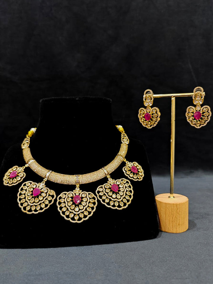 Close-up of an ornate Western American diamond Raizel Ruby Pink Necklace Set (Mehendi Polish) Collar jewellery set and earrings with Colored Stone and American Diamond. Woman styling a statement American diamond necklace with an off-shoulder gown for a reception.