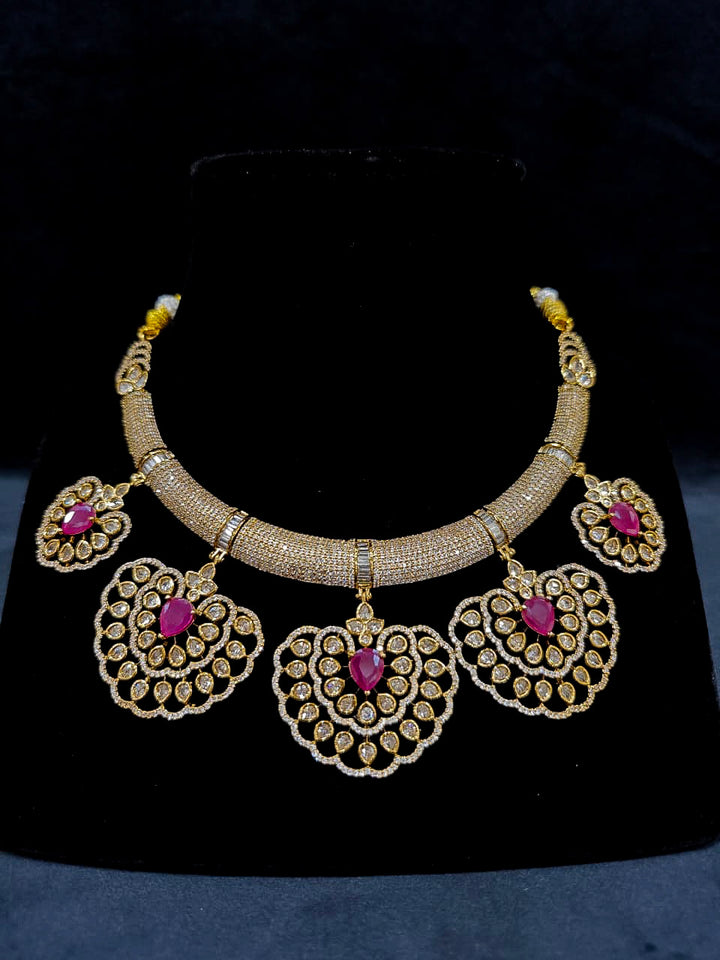 Close-up of an ornate Western American diamond Raizel Ruby Pink Necklace Set (Mehendi Polish) Collar jewellery set and earrings with Colored Stone and American Diamond. Woman styling a statement American diamond necklace with an off-shoulder gown for a reception.