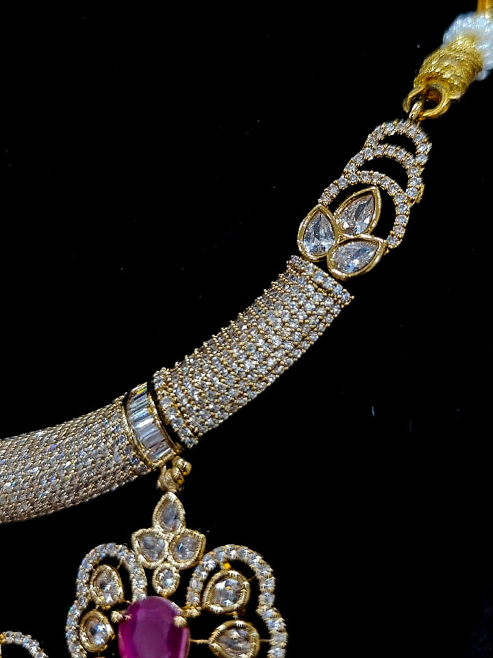Close-up of an ornate Western American diamond Raizel Ruby Pink Necklace Set (Mehendi Polish) Collar jewellery set and earrings with Colored Stone and American Diamond. Woman styling a statement American diamond necklace with an off-shoulder gown for a reception.