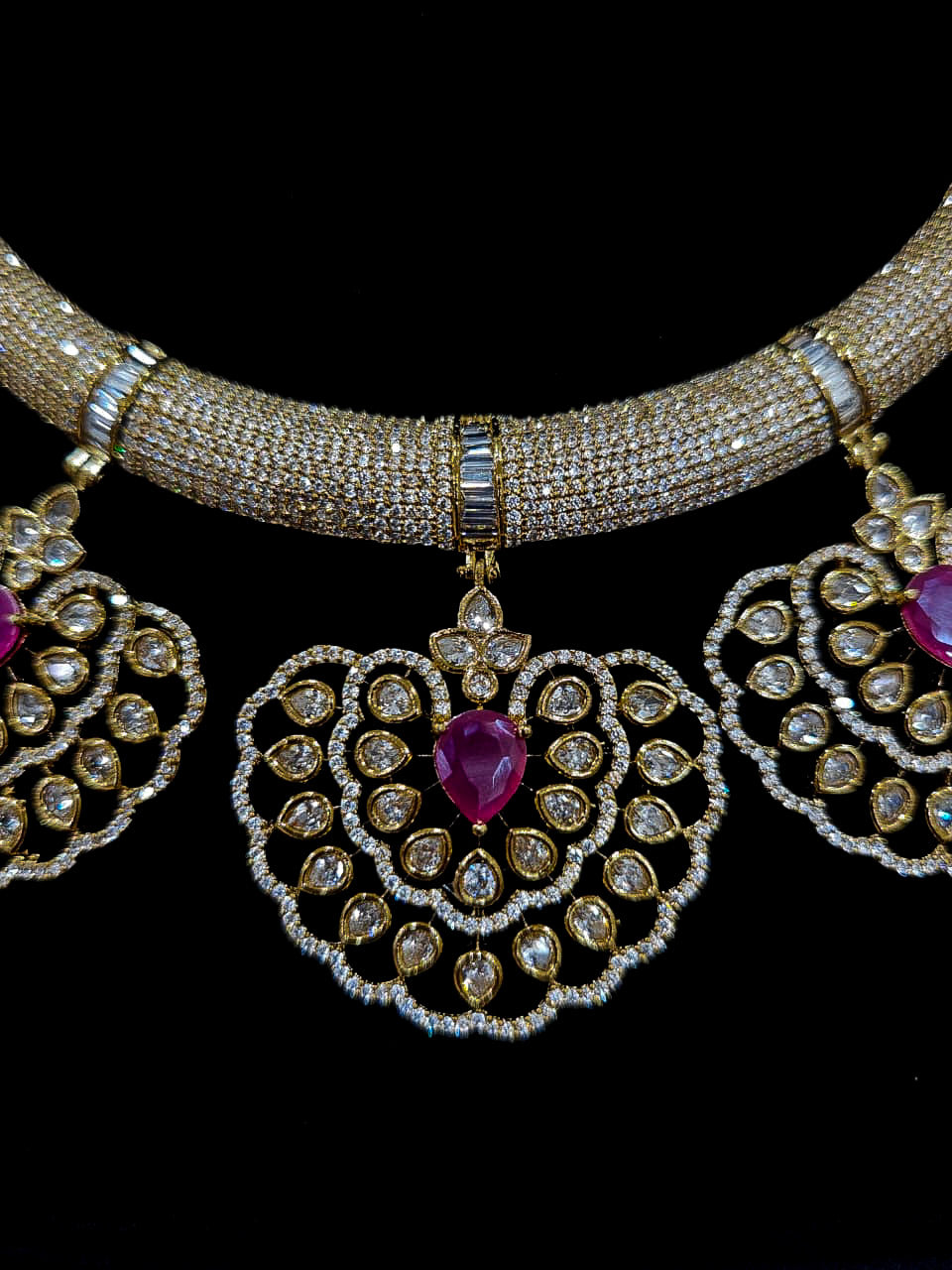 Close-up of an ornate Western American diamond Raizel Ruby Pink Necklace Set (Mehendi Polish) Collar jewellery set and earrings with Colored Stone and American Diamond. Woman styling a statement American diamond necklace with an off-shoulder gown for a reception.