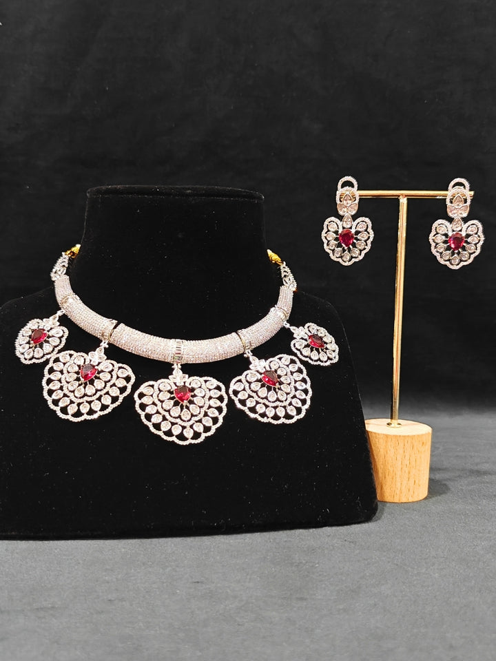 Close-up of an ornate Western American diamond Raizel Ruby Red Necklace Set (Silver Polish) Collar jewellery set and earrings with Colored Stone and American Diamond. Bride-to-be styled in a premium American diamond artificial necklace for her reception party.