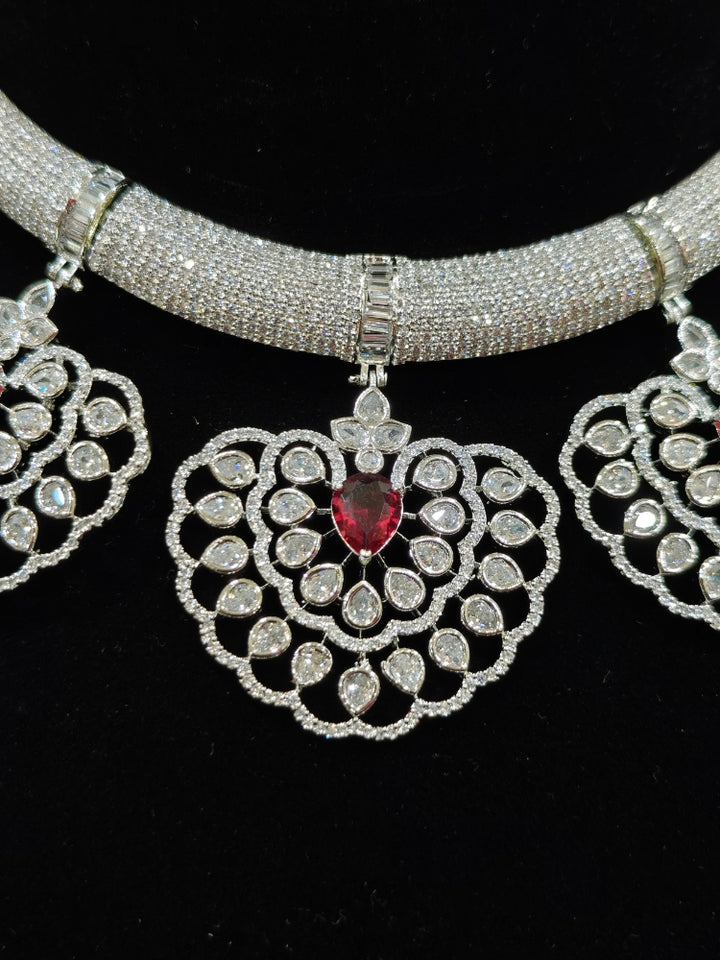 Close-up of an ornate Western American diamond Raizel Ruby Red Necklace Set (Silver Polish) Collar jewellery set and earrings with Colored Stone and American Diamond. Bride-to-be styled in a premium American diamond artificial necklace for her reception party.
