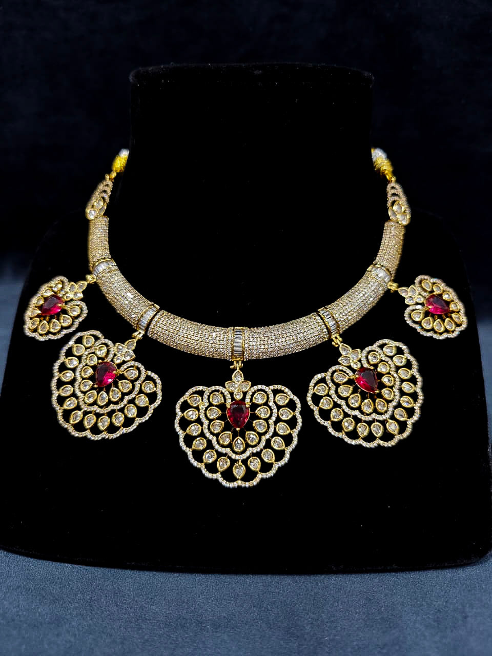 Close-up of an ornate Western American diamond Raizel Ruby red Necklace Set (Mehendi Polish) Collar jewellery set and earrings with Ruby Red Colored Stone and American Diamond. Bride-to-be styled in a premium American diamond artificial necklace for her reception party.