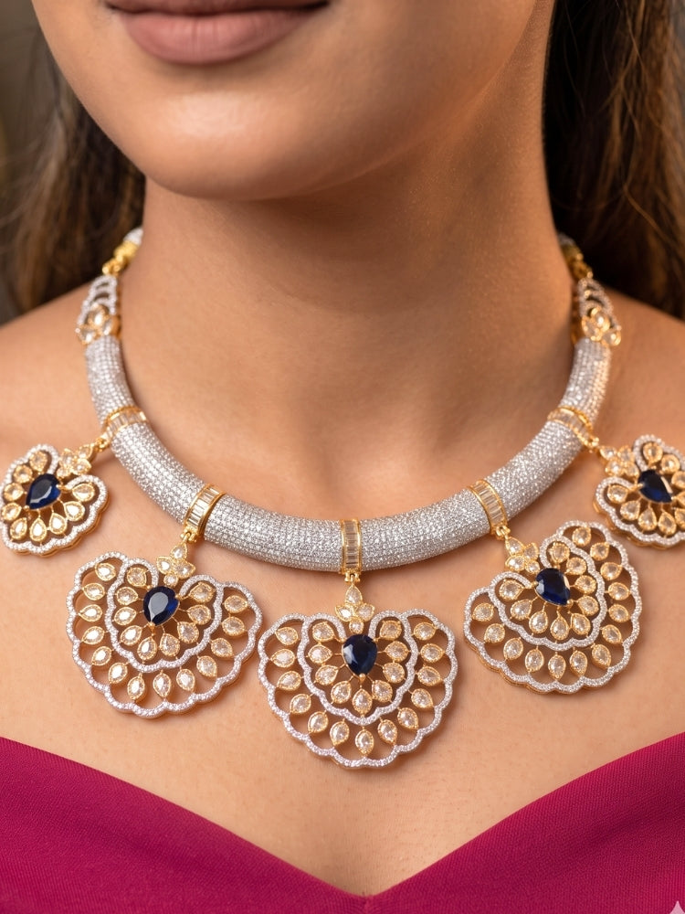 Close-up of a woman wearing an ornate Western American diamond Raizel Blue Necklace Set (Dual Tone) Collar jewellery set and earrings with Colored Stone and American Diamond. Bride-to-be styled in a premium American diamond artificial necklace for her reception party.