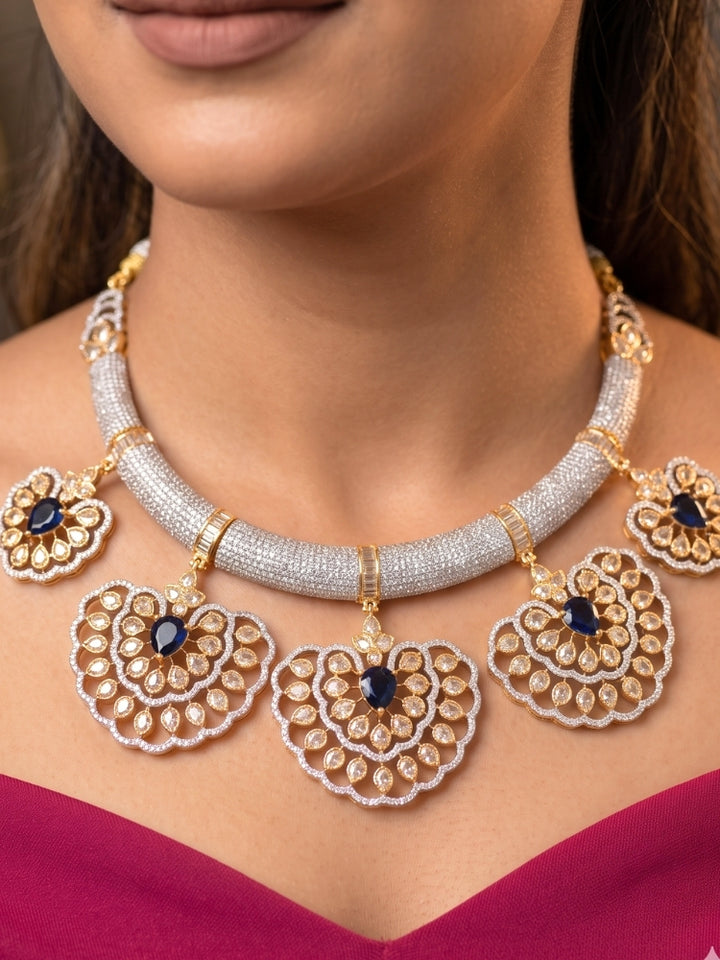 Close-up of a woman wearing an ornate Western American diamond Raizel Blue Necklace Set (Dual Tone) Collar jewellery set and earrings with Colored Stone and American Diamond. Bride-to-be styled in a premium American diamond artificial necklace for her reception party.