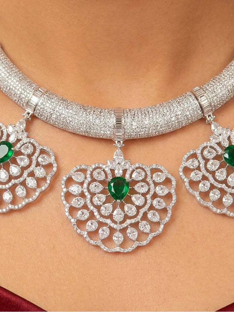 Close-up of a woman wearing an ornate Western American diamond Raizel Emerald Green Necklace Set(Silver Polish) Collar jewellery set and earrings with  Colored Stone and American Diamond. Bride-to-be styled in a premium American diamond artificial necklace for her reception party.