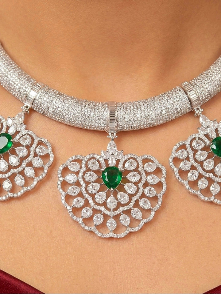 Close-up of a woman wearing an ornate Western American diamond Raizel Emerald Green Necklace Set(Silver Polish) Collar jewellery set and earrings with  Colored Stone and American Diamond. Bride-to-be styled in a premium American diamond artificial necklace for her reception party.