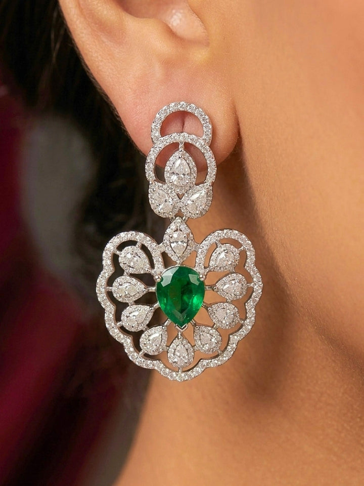 Close-up of a woman wearing an ornate Western American diamond Raizel Emerald Green Necklace Set(Silver Polish) Collar jewellery set and earrings with  Colored Stone and American Diamond. Bride-to-be styled in a premium American diamond artificial necklace for her reception party.