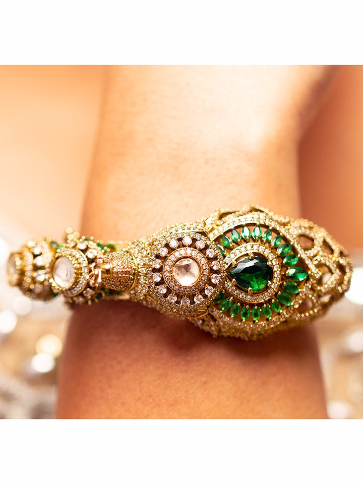 A close-up of the Rajmor Green Bracelet (Openable), featuring ornate gold work, a detailed peacock design with intricate patterns made with sparkling American diamonds and  green colored stones,  worn elegantly on the wrist—perfect as wedding jewelry.
