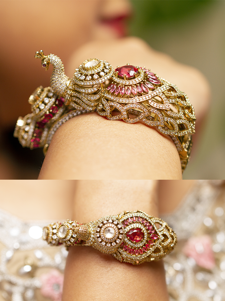 A close-up of the Rajmor Red Bracelet (Openable), featuring ornate gold work, a detailed peacock design with intricate patterns made with sparkling American diamonds and  Red colored stones,  worn elegantly on the wrist—perfect as wedding jewelry.