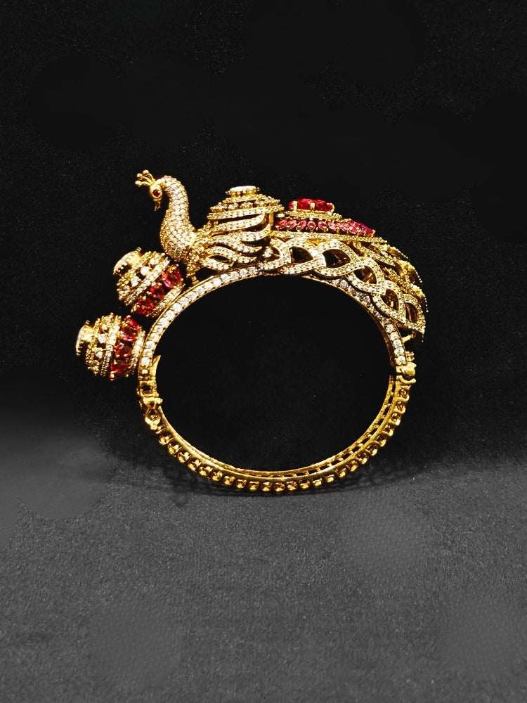 A close-up of the Rajmor Red Bracelet (Openable), featuring ornate gold work, a detailed peacock design with intricate patterns made with sparkling American diamonds and  Red colored stones,  worn elegantly on the wrist—perfect as wedding jewelry.