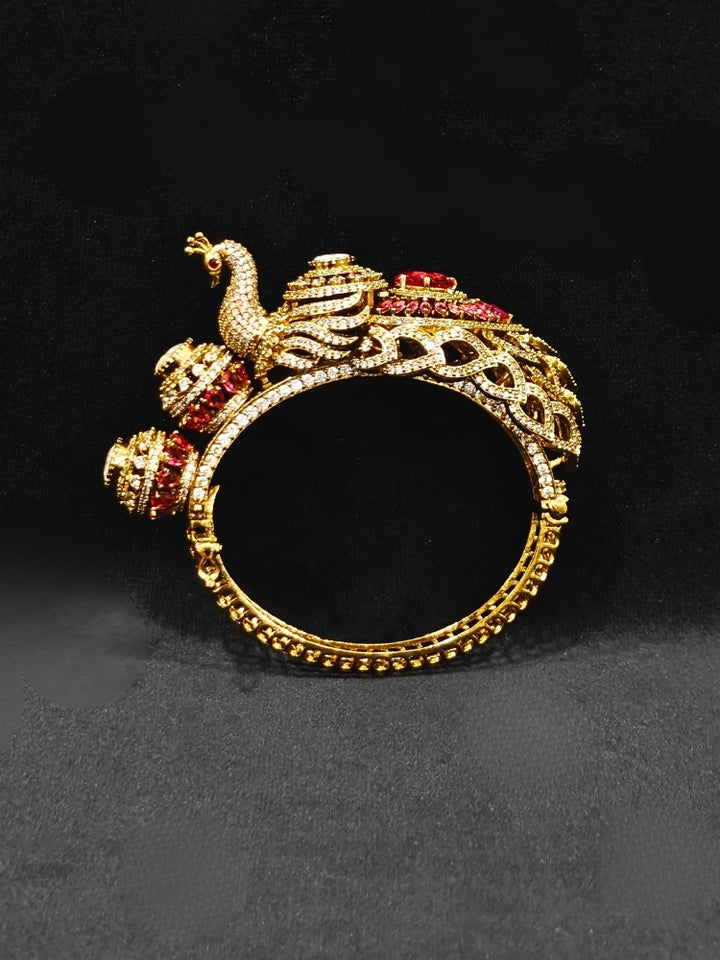 A close-up of the Rajmor Red Bracelet (Openable), featuring ornate gold work, a detailed peacock design with intricate patterns made with sparkling American diamonds and  Red colored stones,  worn elegantly on the wrist—perfect as wedding jewelry.