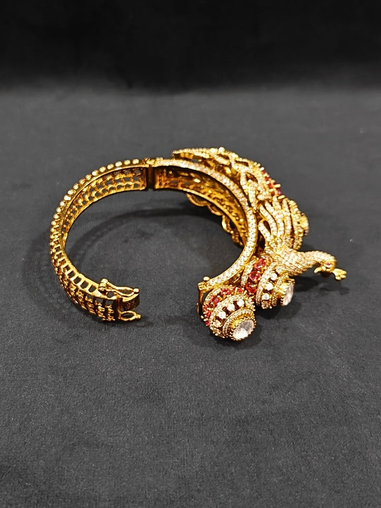 A close-up of the Rajmor Red Bracelet (Openable), featuring ornate gold work, a detailed peacock design with intricate patterns made with sparkling American diamonds and  Red colored stones,  worn elegantly on the wrist—perfect as wedding jewelry.