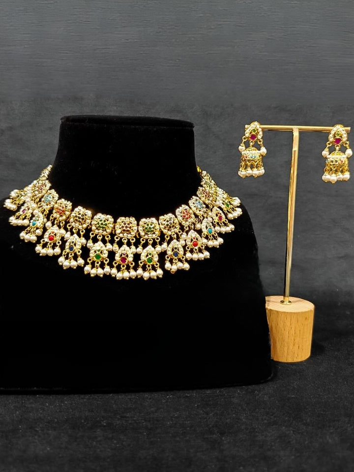 Close-up of an ornate traditional Navratan jadau gold jewellery set and jadau earrings with Pearls and Navratan Stones. Elegant reception look featuring a luxury Jadau artificial jewelry set. Festive celebration look featuring a Jadau artificial necklace.