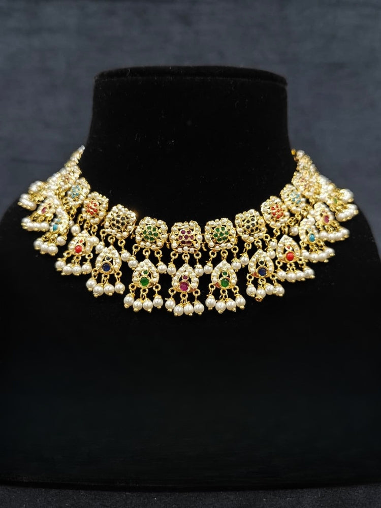Close-up of an ornate traditional Navratan jadau gold jewellery set and jadau earrings with Pearls and Navratan Stones. Elegant reception look featuring a luxury Jadau artificial jewelry set. Festive celebration look featuring a Jadau artificial necklace.