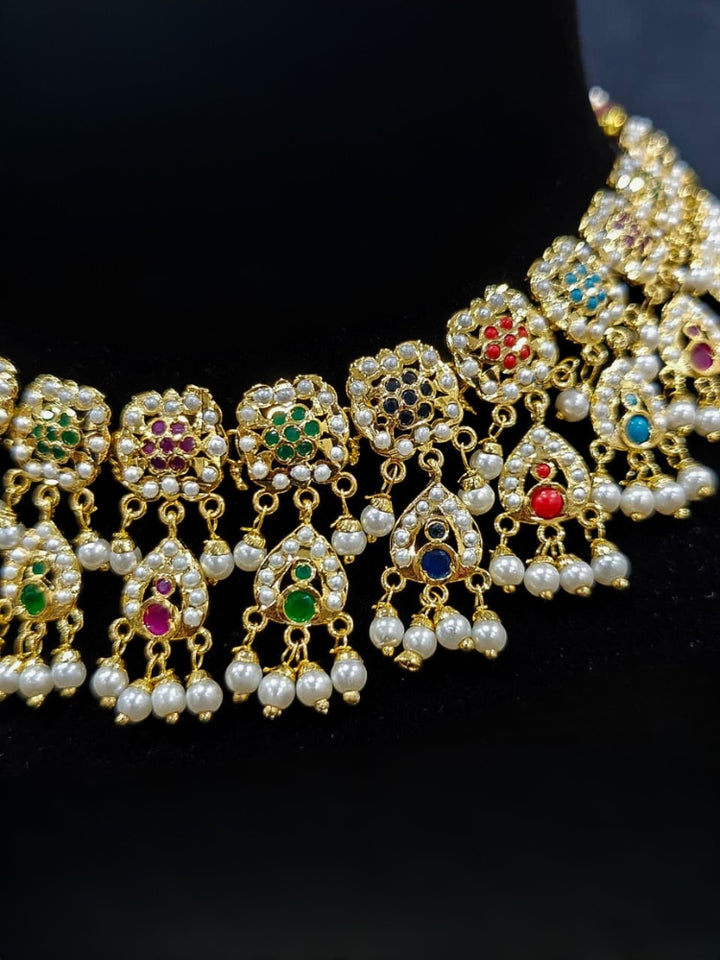 Close-up of an ornate traditional Navratan jadau gold jewellery set and jadau earrings with Pearls and Navratan Stones. Elegant reception look featuring a luxury Jadau artificial jewelry set. Festive celebration look featuring a Jadau artificial necklace.
