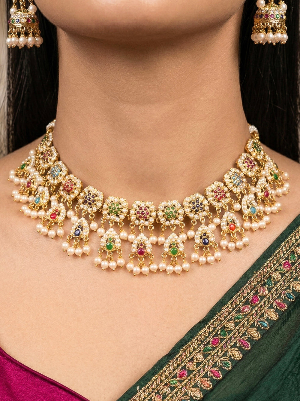 Close-up of a woman wearing an ornate traditional Navratan jadau gold jewellery set and jadau earrings with Pearls and Navratan Stones. Woman pairing a traditional Jadau necklace with a silk saree. Woman wearing a premium Jadau artificial jewelry set for reception night.