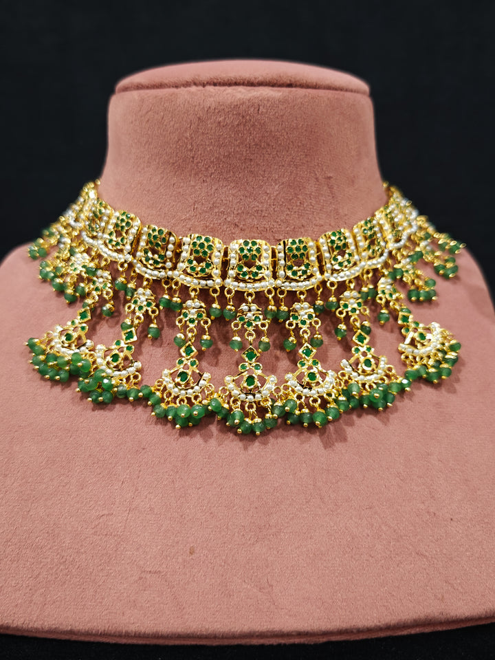Close-up of an ornate traditional jadau gold jewellery set and jadau earrings with Beads and gemstones. Woman pairing a traditional Jadau necklace with a silk saree.Woman wearing a royal Jadau necklace for festive events in India.
