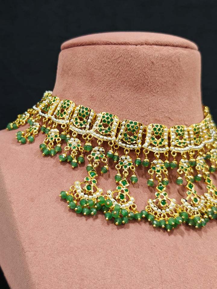 Close-up of an ornate traditional jadau gold jewellery set and jadau earrings with Beads and gemstones. Woman pairing a traditional Jadau necklace with a silk saree.Woman wearing a royal Jadau necklace for festive events in India.