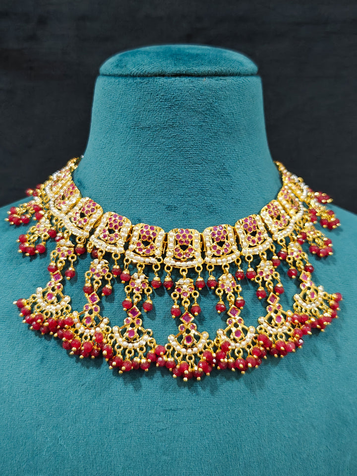 Close-up of an ornate traditional Ruby Pink jadau gold jewellery set and jadau earrings with Beads and gemstones. Close-up of a luxury Jadau imitation necklace styled with a bridal lehenga .Statement Jadau necklace styled for a wedding guest outfit.
