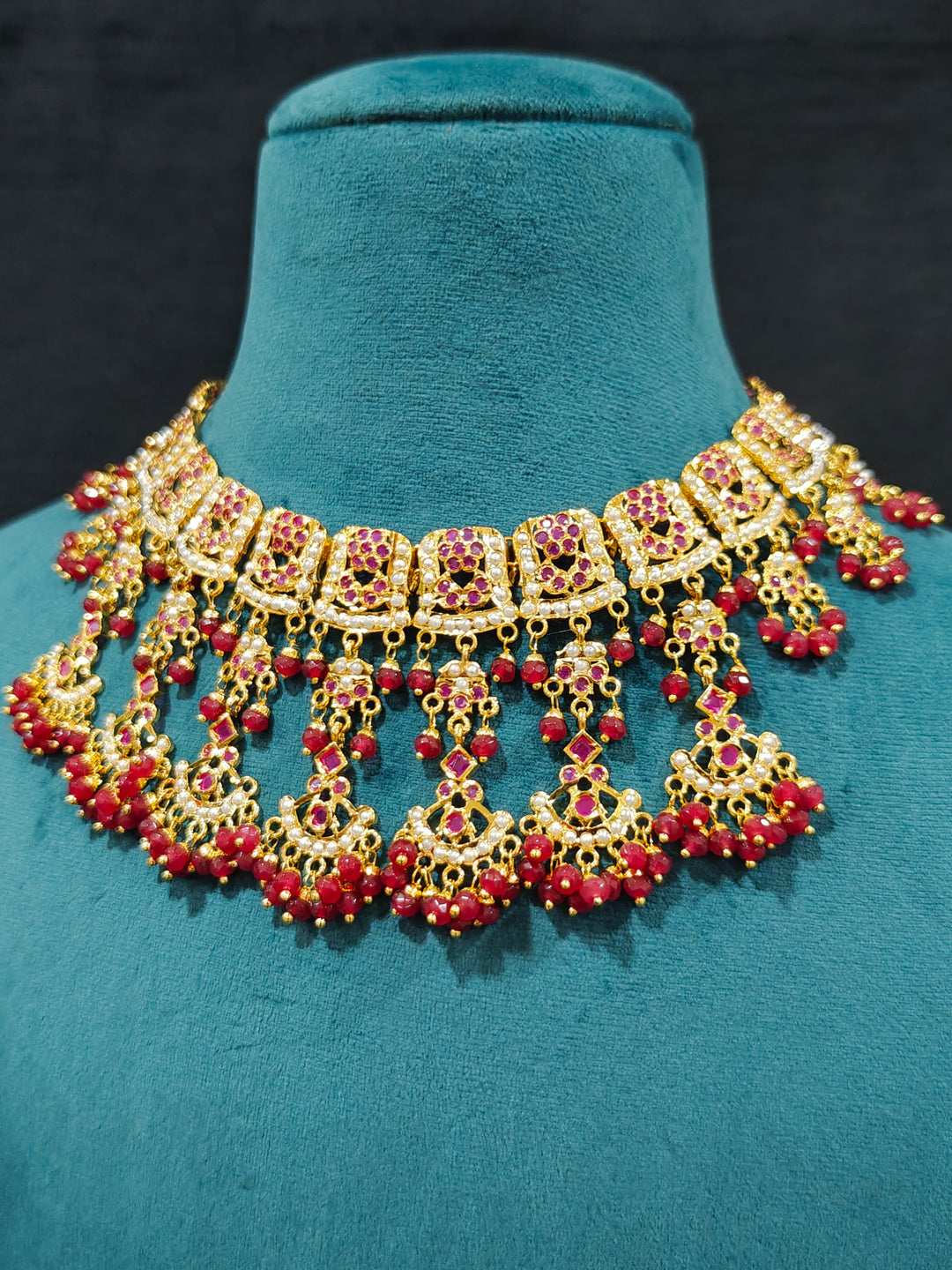 Close-up of an ornate traditional Ruby Pink jadau gold jewellery set and jadau earrings with Beads and gemstones. Close-up of a luxury Jadau imitation necklace styled with a bridal lehenga .Statement Jadau necklace styled for a wedding guest outfit.